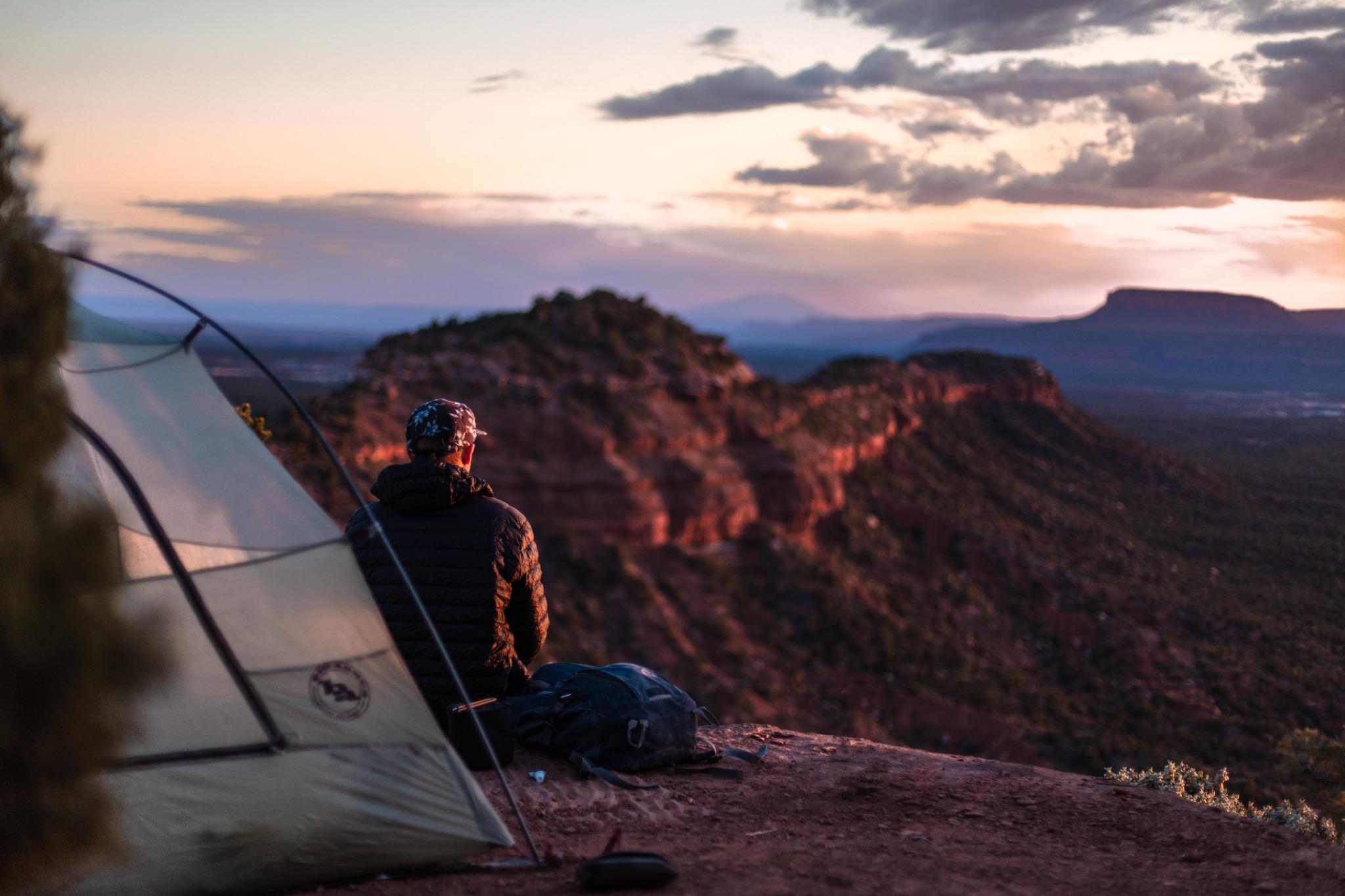 Camper sitting beside a tent overlooking a desert valley at sunset