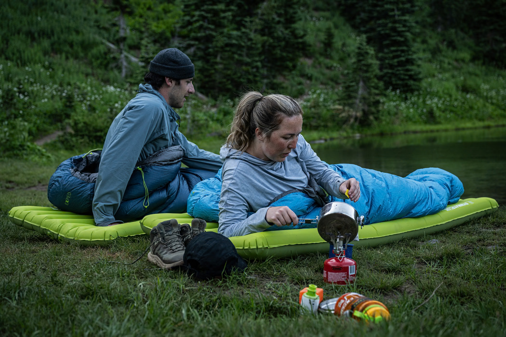 Exped mat beneath a camper's sleeping bag beside a lakeside camp