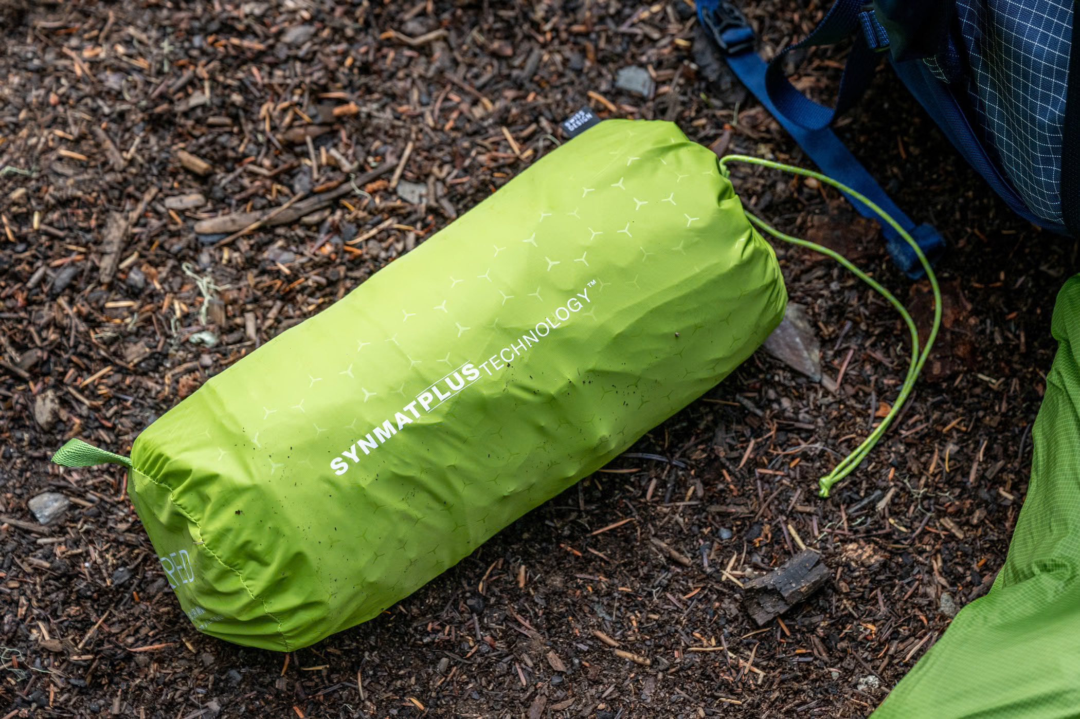 Lime-green Exped Ultra sleeping mat packed into its stuff sack on a campsite floor