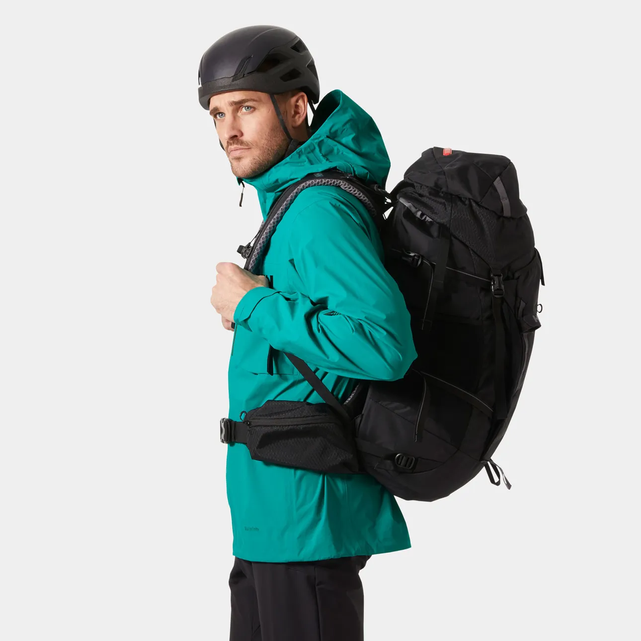 Side view of the Helly Hansen Odin Ultimate Infinity Shell Jacket worn with a large backpack