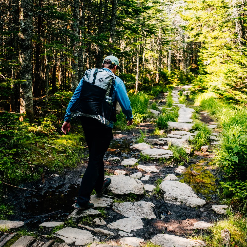Hiker wearing a black Hyperlite Mountain Gear Unbound 40 on a forest trail