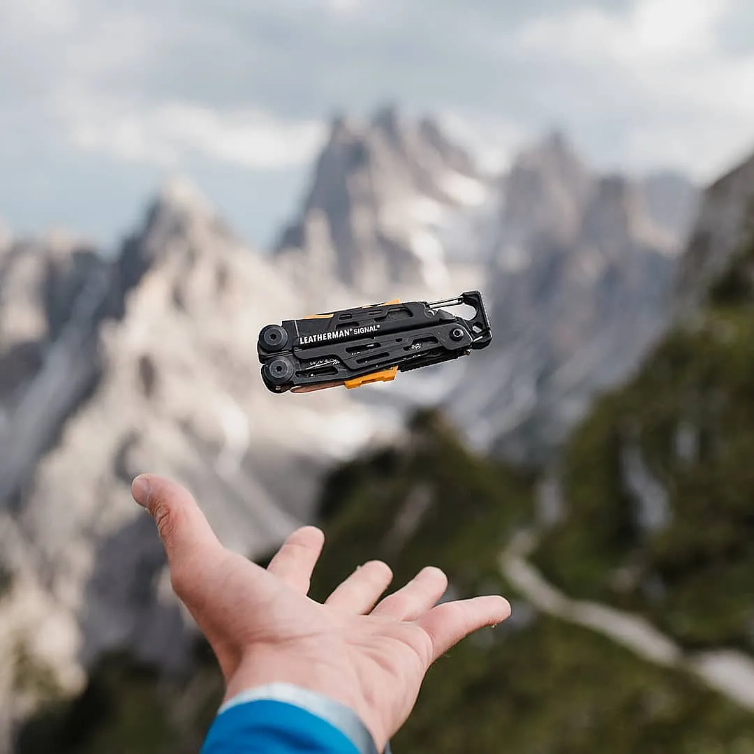 Black and orange Leatherman Signal suspended above a hand in the mountains