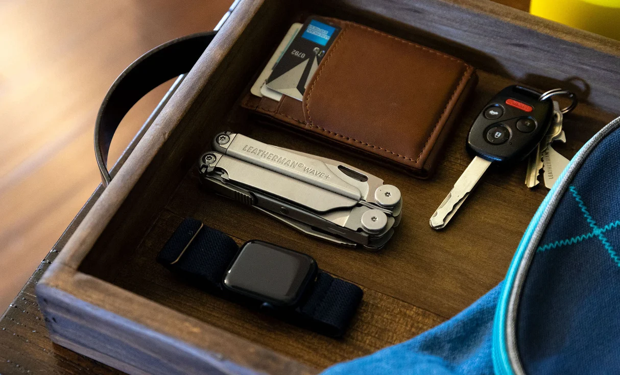 Closed stainless Leatherman Wave+ beside wallet and keys in a tray