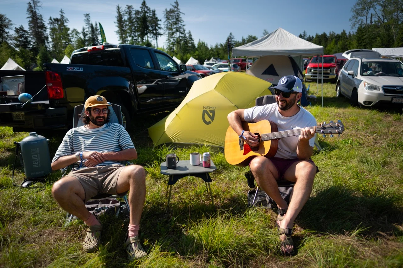 Two campers seated beside a tent at a grassy campsite