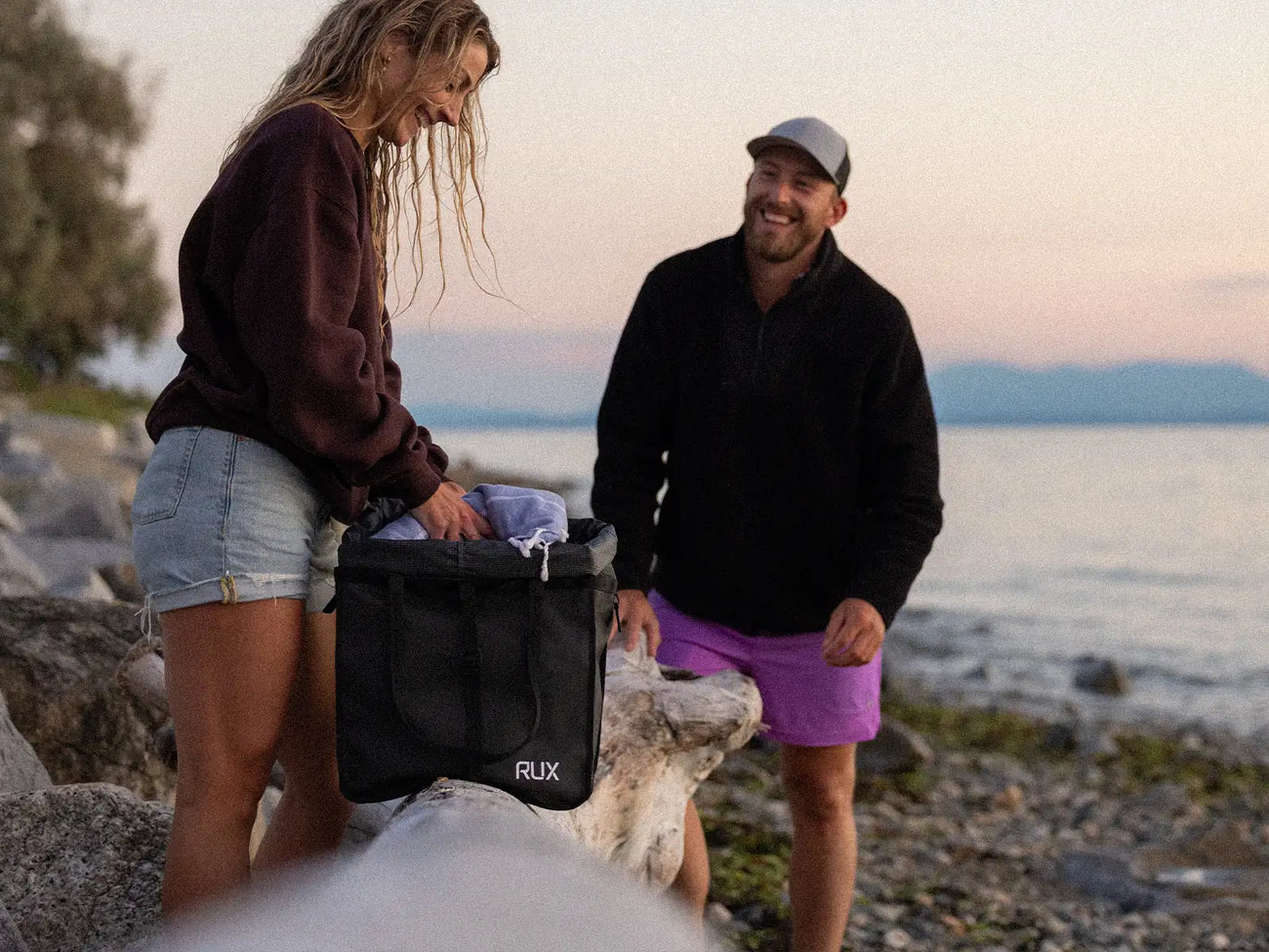 A RUX Bag 25L being loaded with clothes beside the water