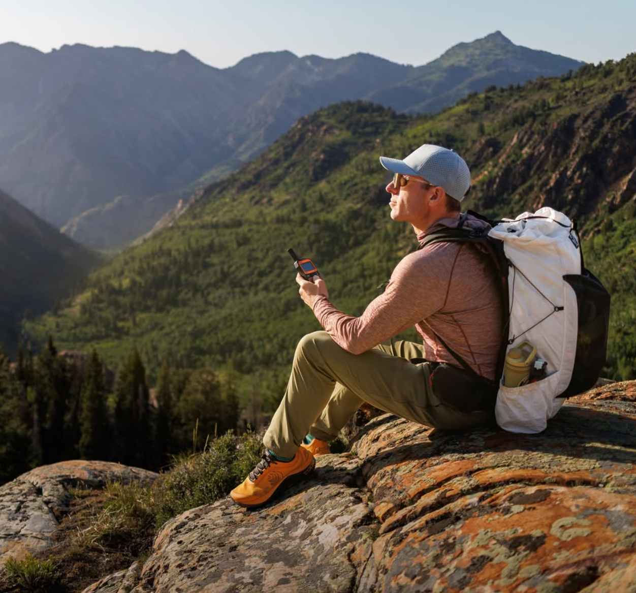 Hiker holding SPOT X while resting above a valley