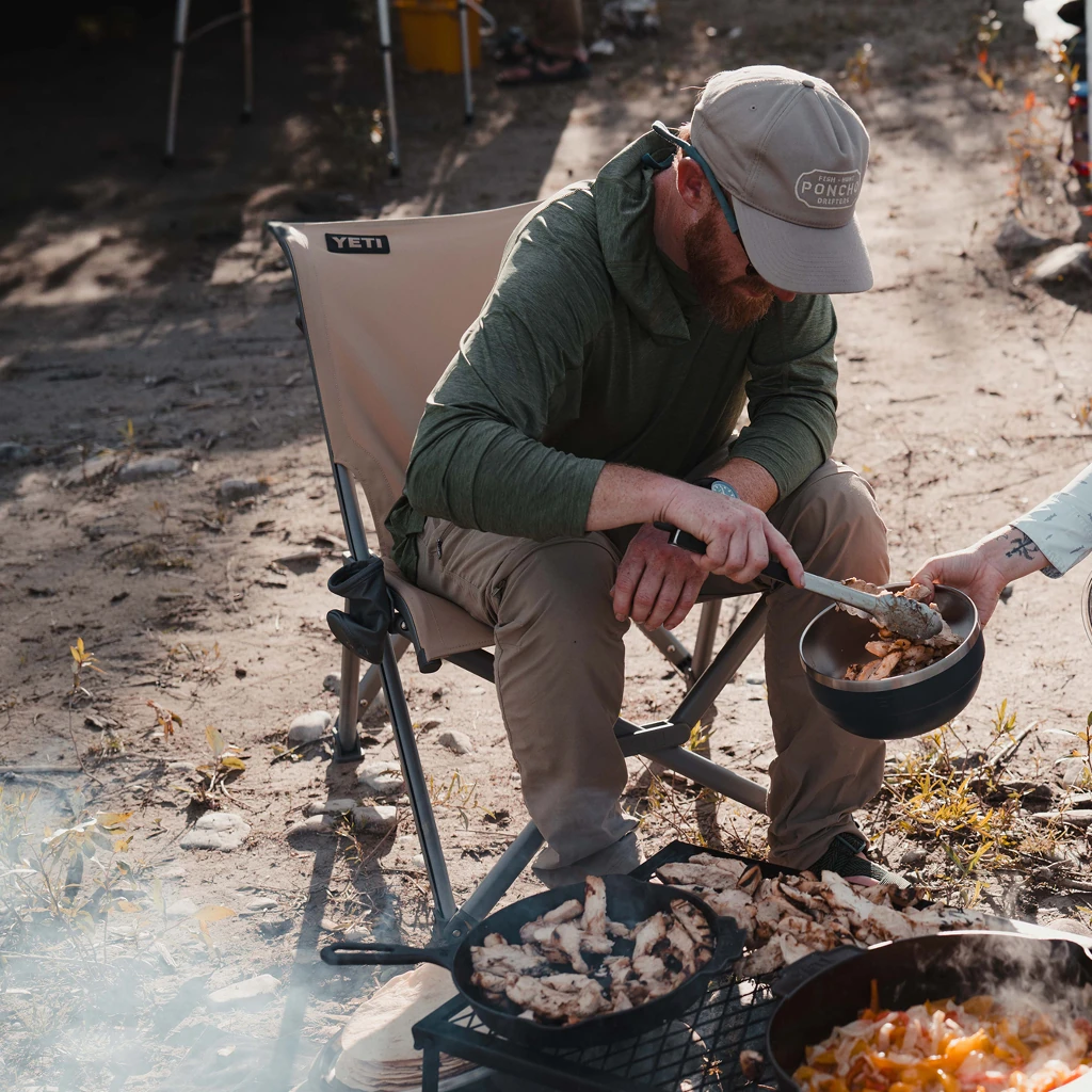 Camper sitting in the Trailhead Field Chair beside a cooking fire