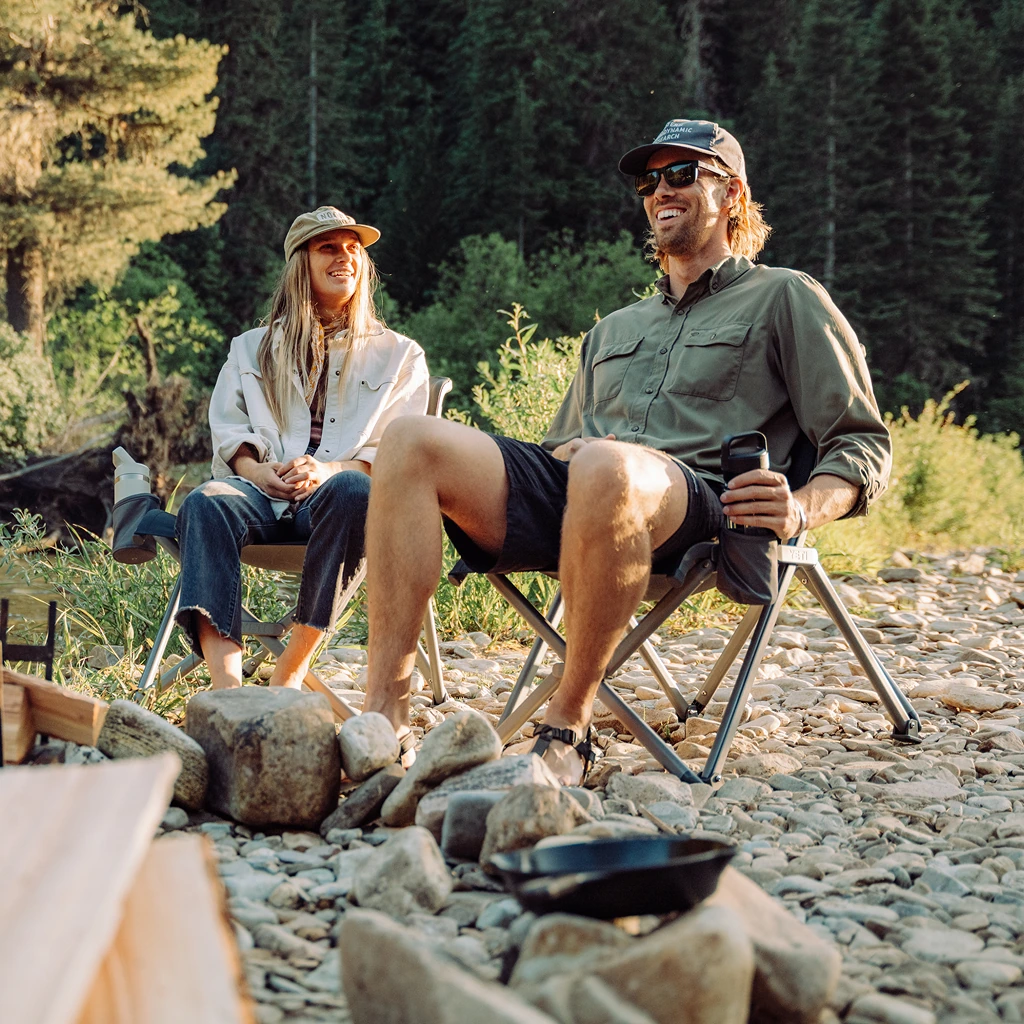 Two campers sitting on rocky ground beside a fire
